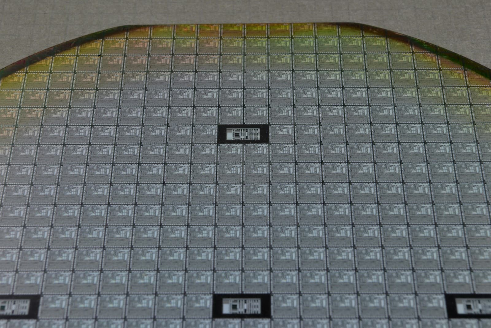 Macro of a silicon wafer, its grid of chips catching the light along the curved edge.